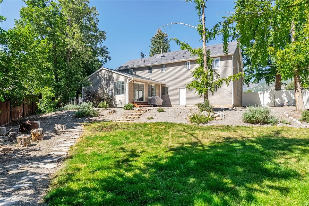Expansive backyard featuring a manicured lawn, established trees, and a stone-paver pathway