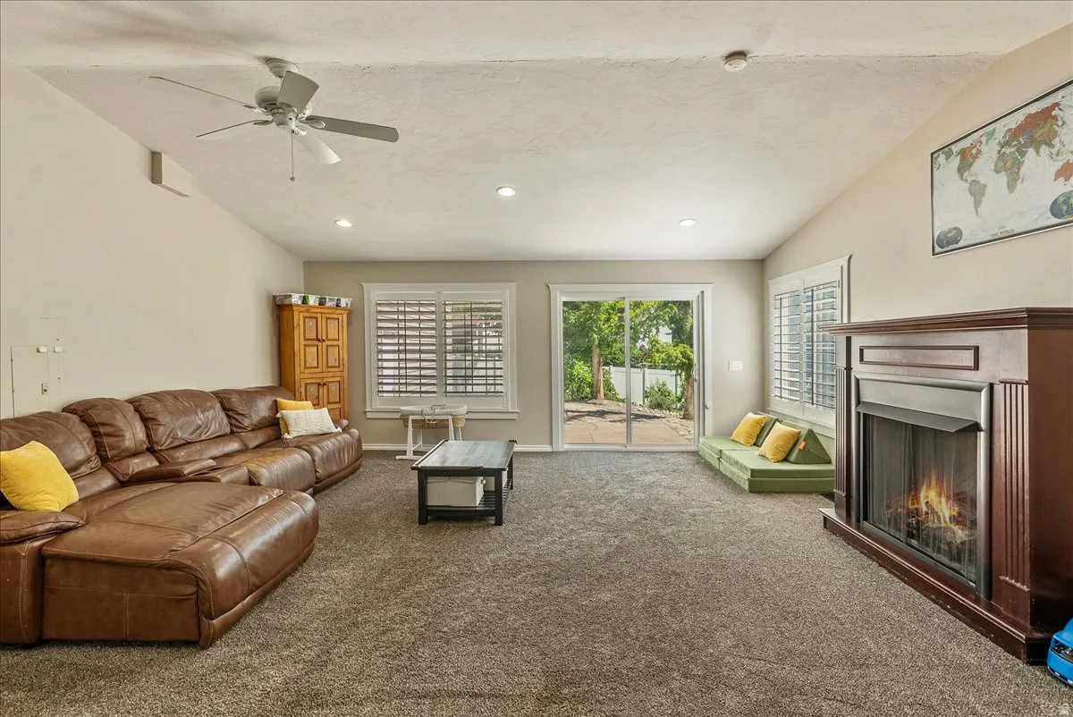 Vaulted ceiling featuring a ceiling fan, recessed lighting, and an integrated fireplace with a wood-finish mantel