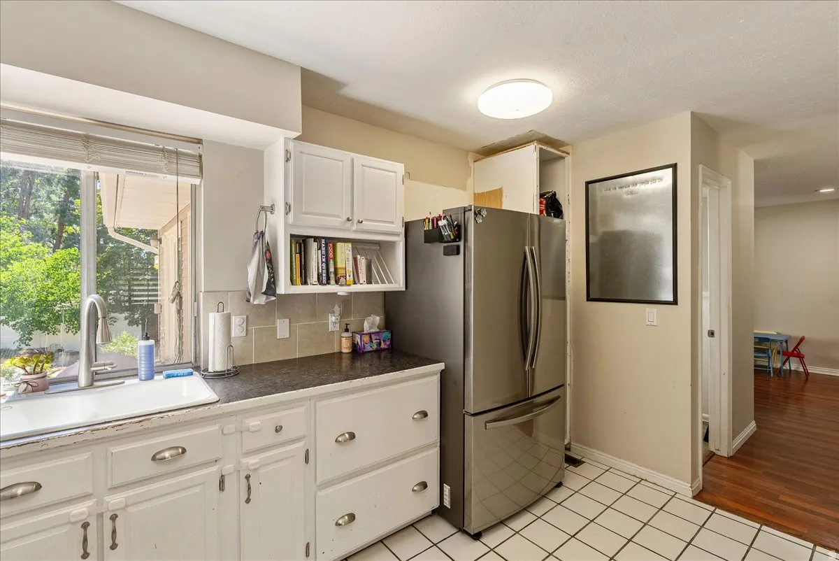 Kitchen featuring a stainless steel refrigerator, white cabinetry, dark countertops, a window over the sink, and tiled flooring