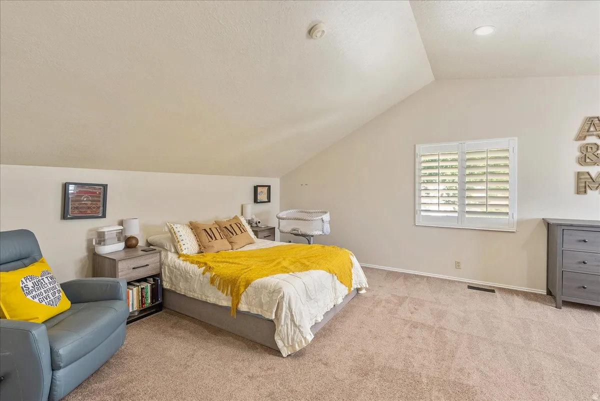 Vaulted ceiling with recessed lighting, carpet flooring, and a window with white plantation shutters