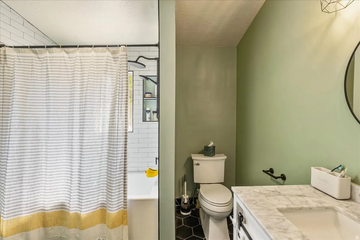 Bathroom featuring a white subway tile shower, built-in shower shelving, hexagonal floor tiles, a toilet, and a vanity with a white countertop