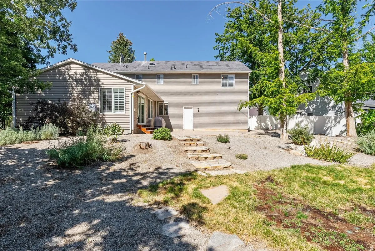 Rear exterior featuring siding, multiple windows, stone steps, a white exterior door, and established trees