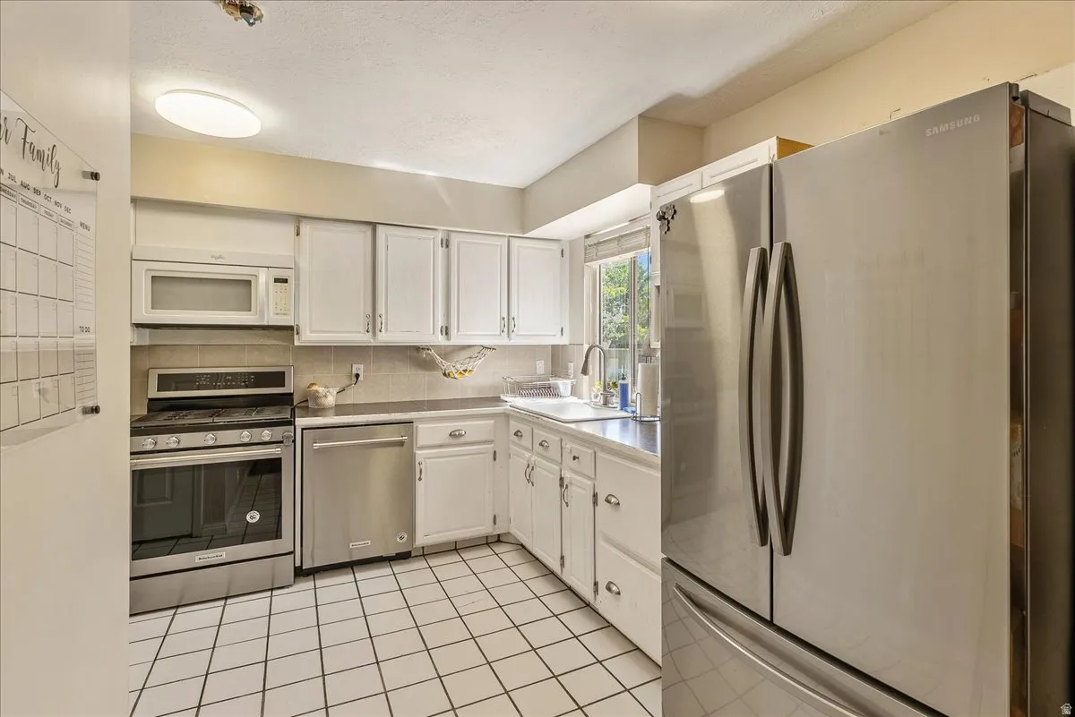 White cabinetry with silver-tone hardware, stainless steel appliances, tiled backsplash, and tiled flooring