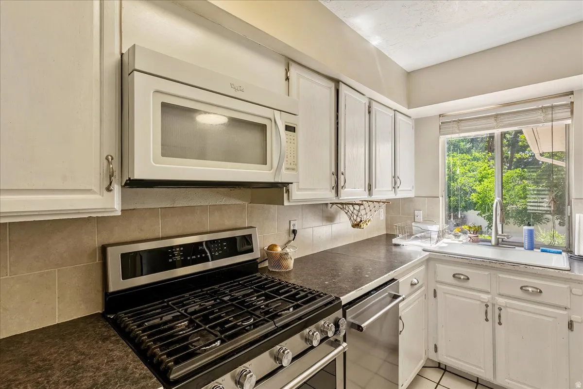 Kitchen featuring white cabinetry, tile backsplash, stainless steel gas range, over-the-range microwave, and a window above the sink
