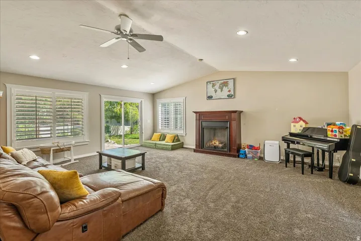 Vaulted ceiling with a ceiling fan and recessed lighting, brown wood-finish fireplace, and sliding glass door leading to a patio