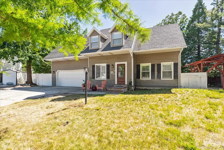 Gabled roofline with dormer windows, attached garage, wood-finish siding, white window shutters, and a covered front entry