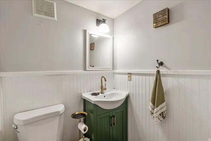 White beadboard wainscoting, wall-mounted mirror, and vanity with integrated sink and brass-finish faucet