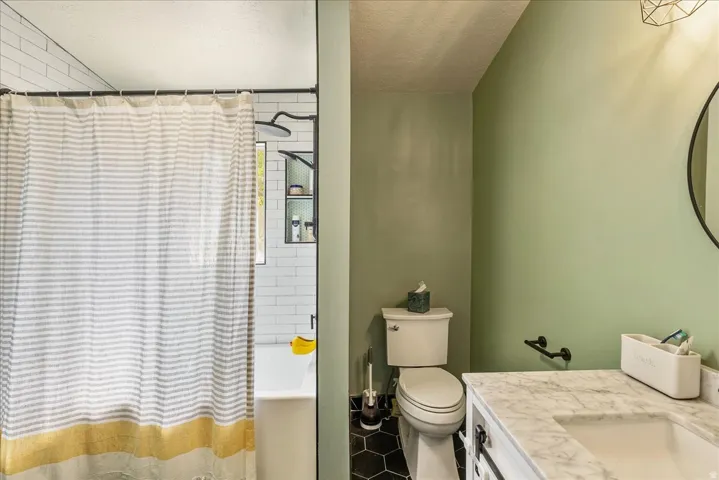 Bathroom featuring a white subway tile shower, built-in shower shelving, hexagonal floor tiles, a toilet, and a vanity with a white countertop