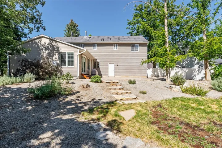Rear exterior featuring siding, multiple windows, stone steps, a white exterior door, and established trees