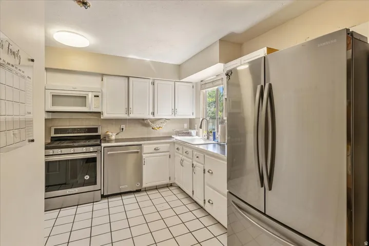 White cabinetry with silver-tone hardware, stainless steel appliances, tiled backsplash, and tiled flooring