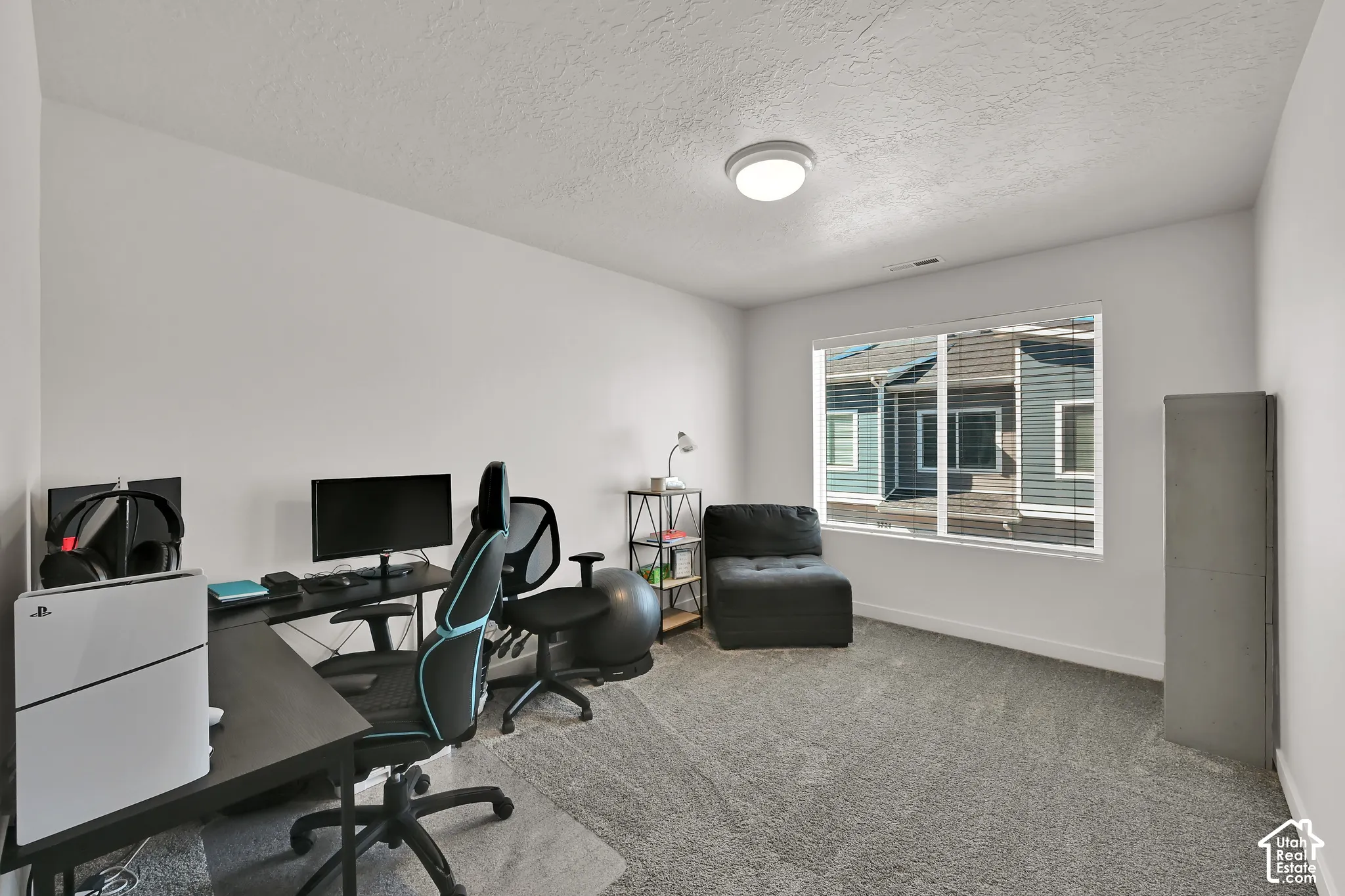 White wall paint, textured ceiling, large window with blinds, recessed lighting fixture, and gray carpeting