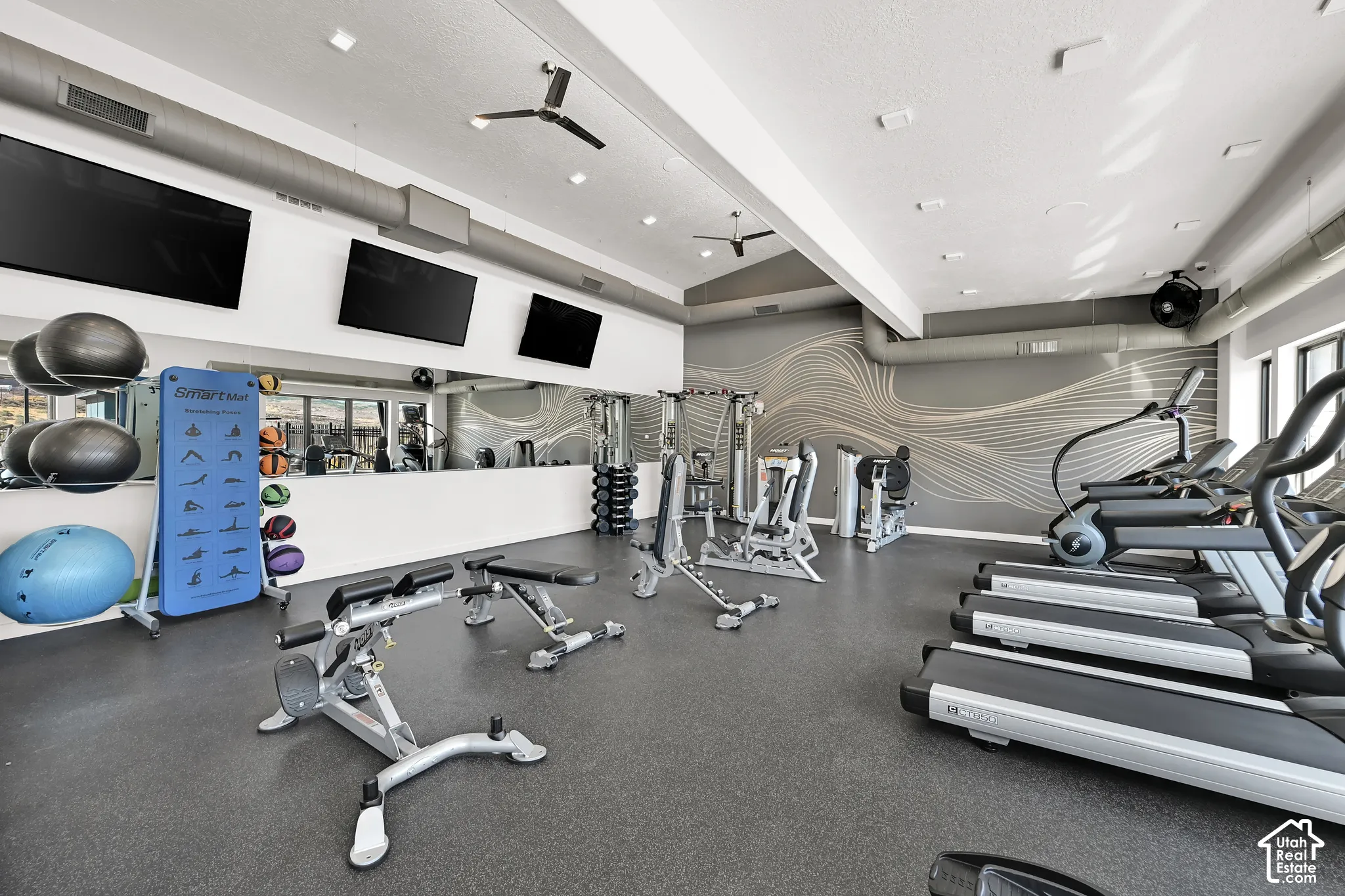 Fitness center with rubber flooring, three ceiling fans, wall-mounted televisions, and a mirrored wall