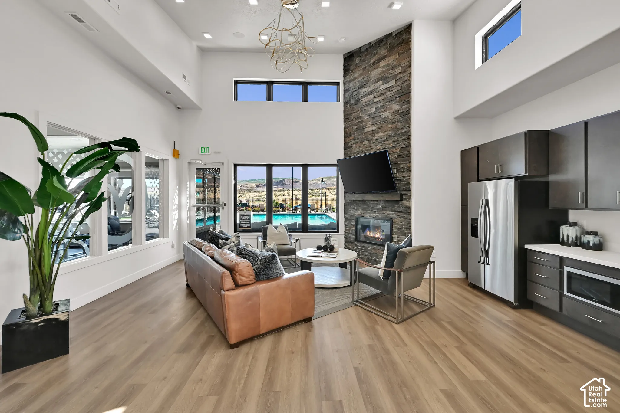 Vaulted ceilings with clerestory windows, wood-finish flooring, a stacked stone fireplace, stainless steel appliances, and dark wood-finish cabinetry with light countertops