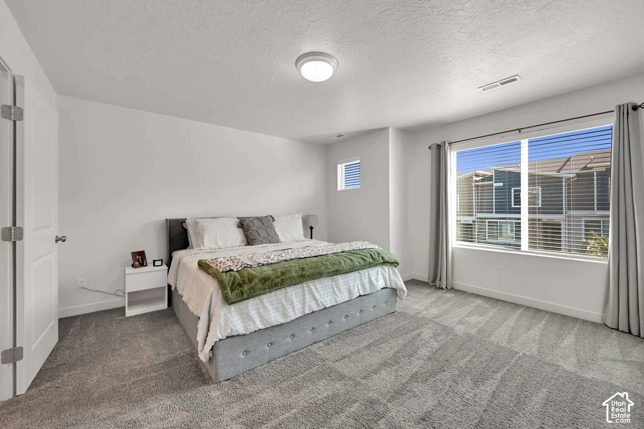Wall-to-wall carpeting, large window with blinds, overhead flush-mount lighting, and white interior doors