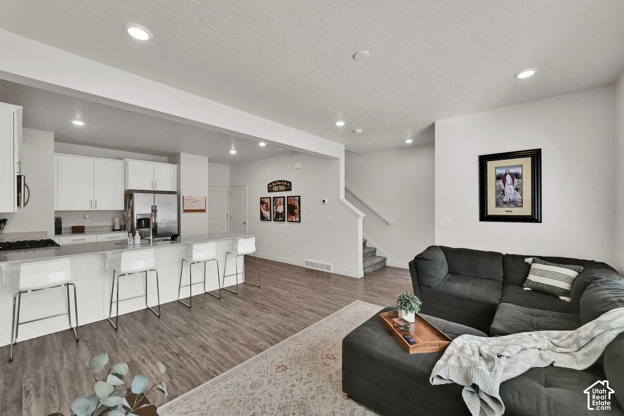 Open-concept living area with wood-finish flooring, recessed lighting, and a white kitchen featuring stainless steel appliances