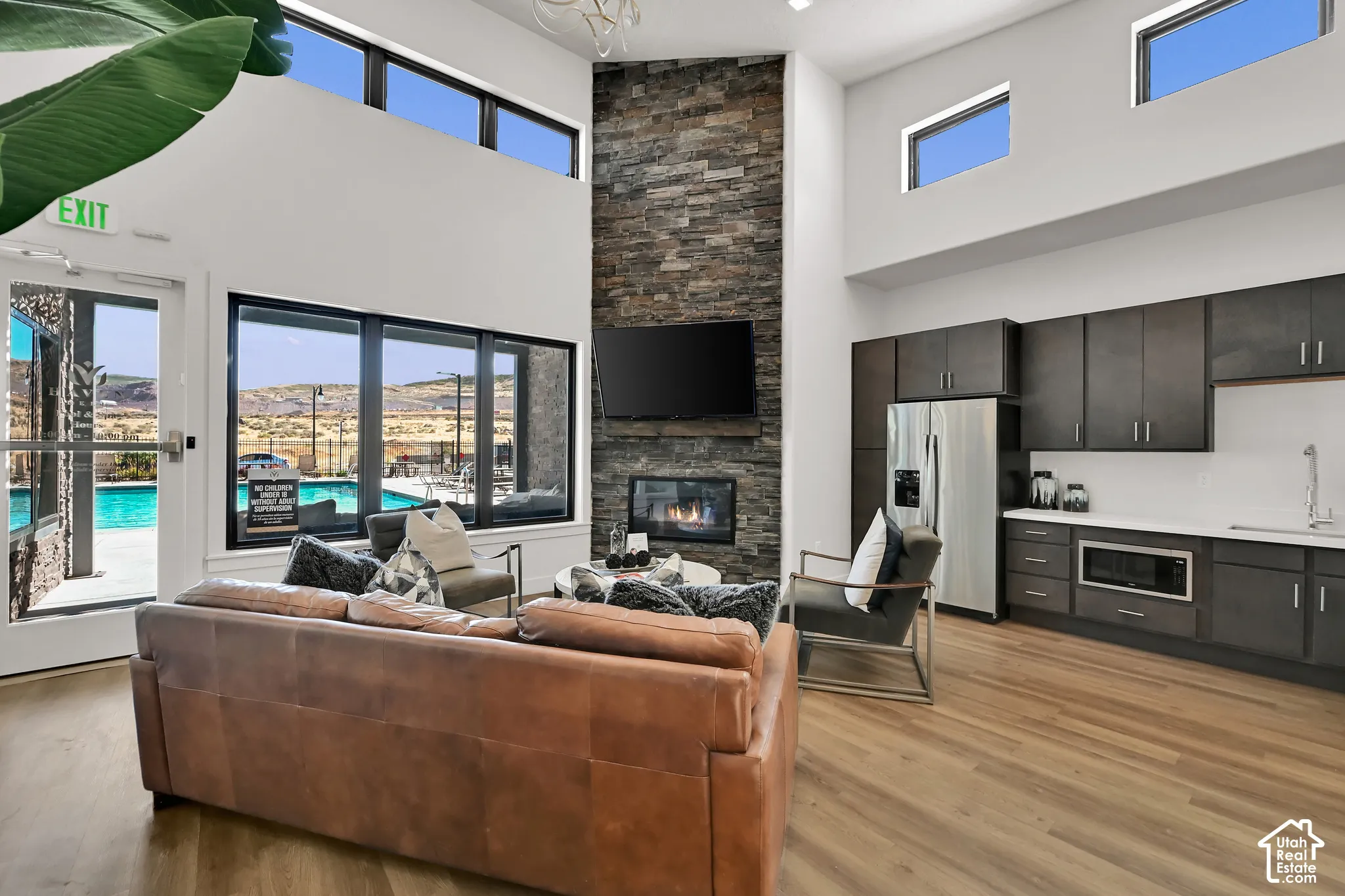 Vaulted ceilings with clerestory windows, floor-to-ceiling stone-clad fireplace with hearth, stainless steel appliances, modern cabinetry with integrated sink, and wood-finish flooring