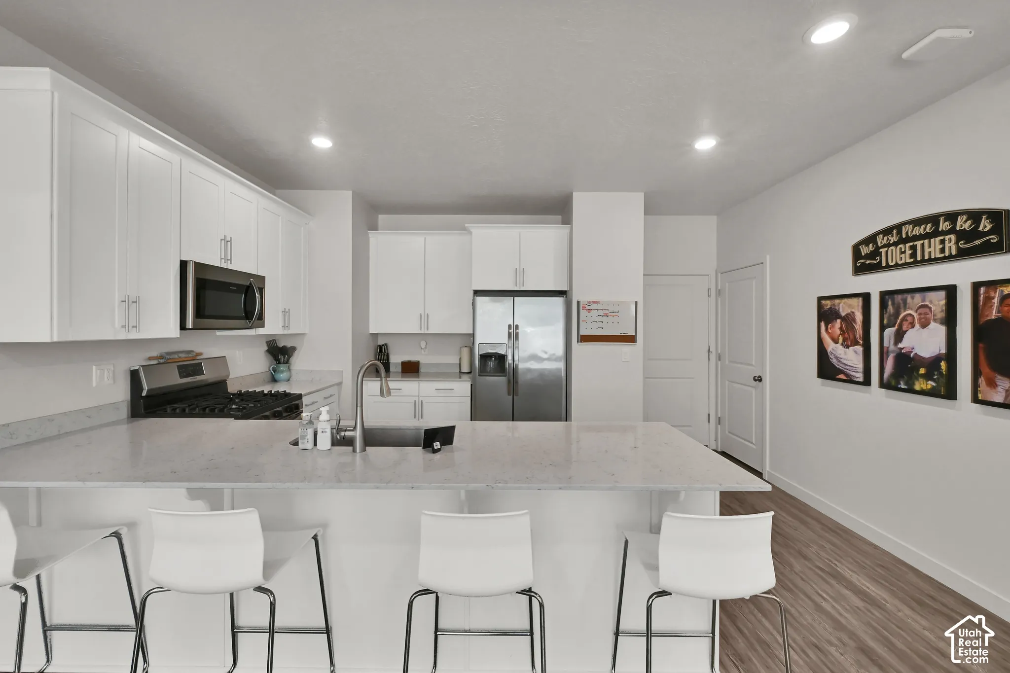 White shaker cabinetry, stainless steel appliances, light-toned countertops, recessed lighting, and wood-finish flooring