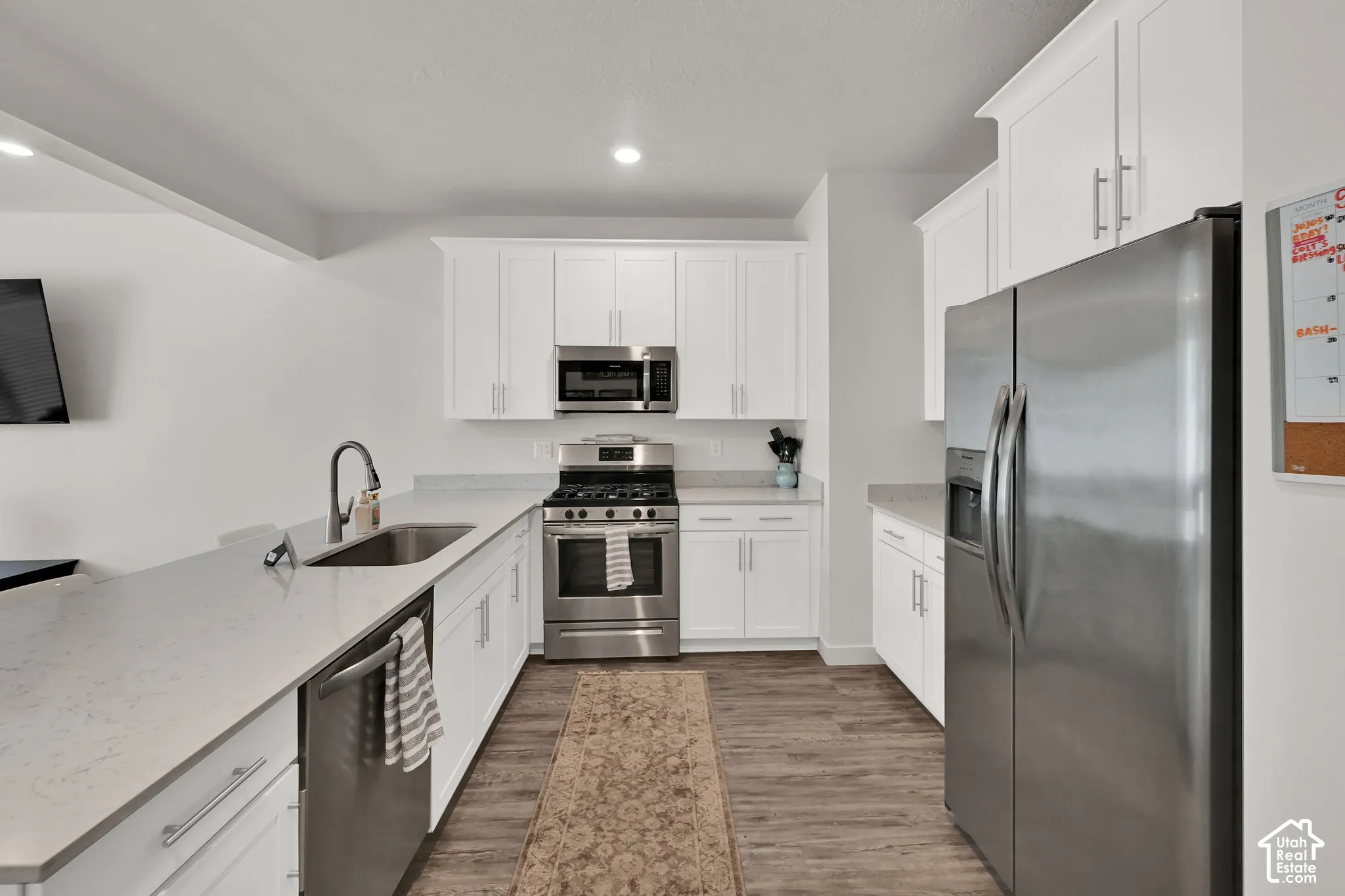 White shaker cabinetry, stainless steel appliances, light-toned countertops, undermount sink, and wood-finish flooring