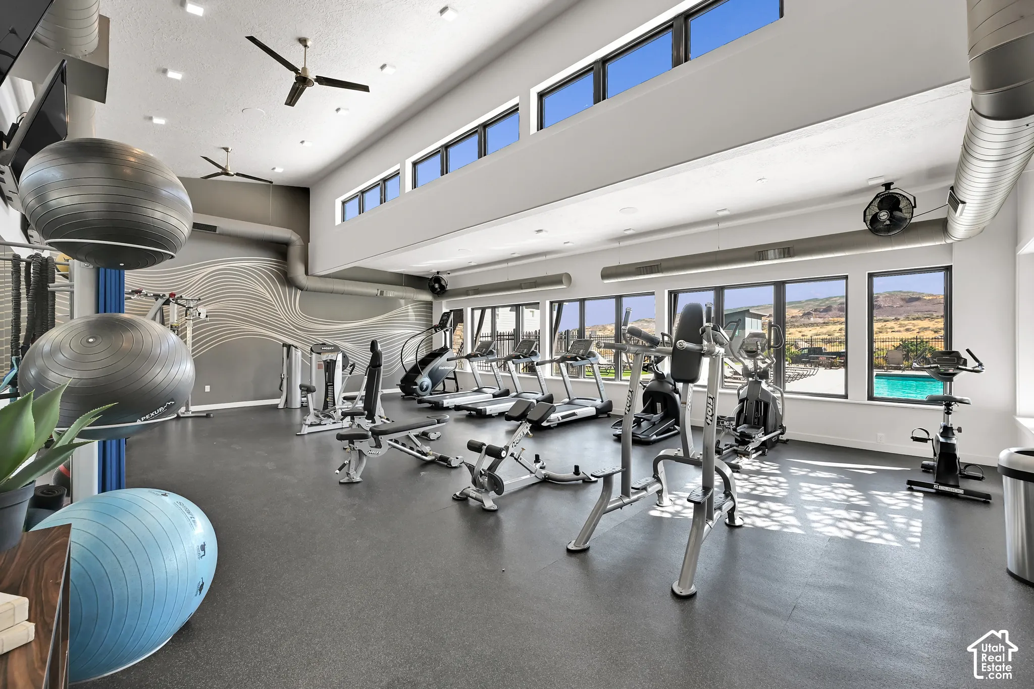 Fitness facility featuring a high ceiling, multiple large windows, exposed ductwork, and ceiling fans