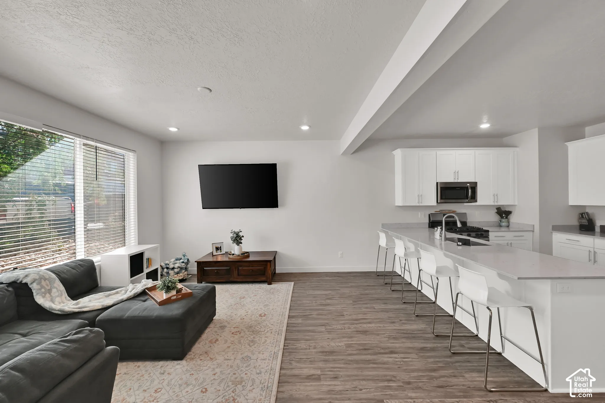 Open-concept living space featuring wood-finish flooring, recessed lighting, and a large window