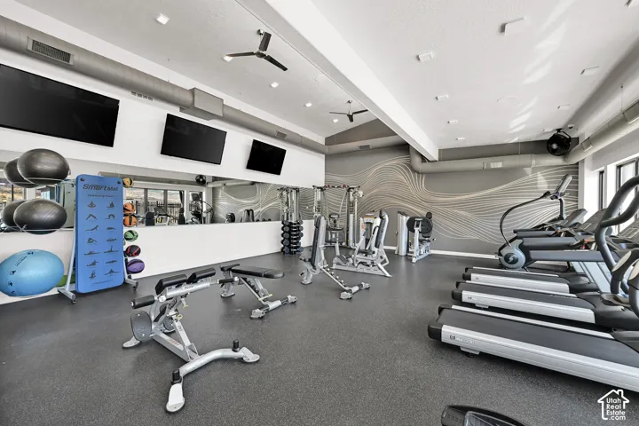 Fitness center with rubber flooring, three ceiling fans, wall-mounted televisions, and a mirrored wall