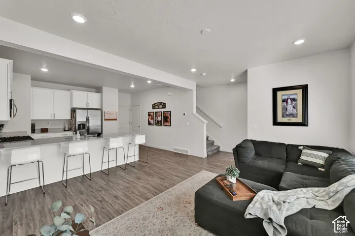 Open-concept living area with wood-finish flooring, recessed lighting, and a white kitchen featuring stainless steel appliances