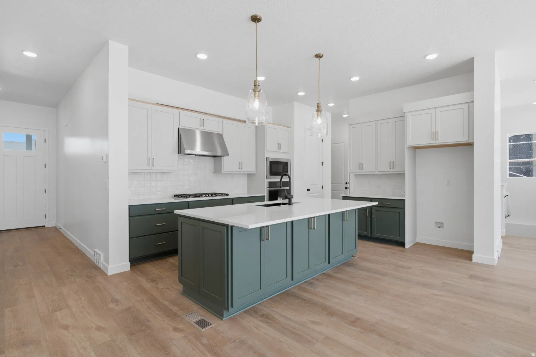 Open-concept kitchen featuring an expansive island with a light-toned countertop, two-tone cabinetry, wood-finish flooring, and recessed lighting