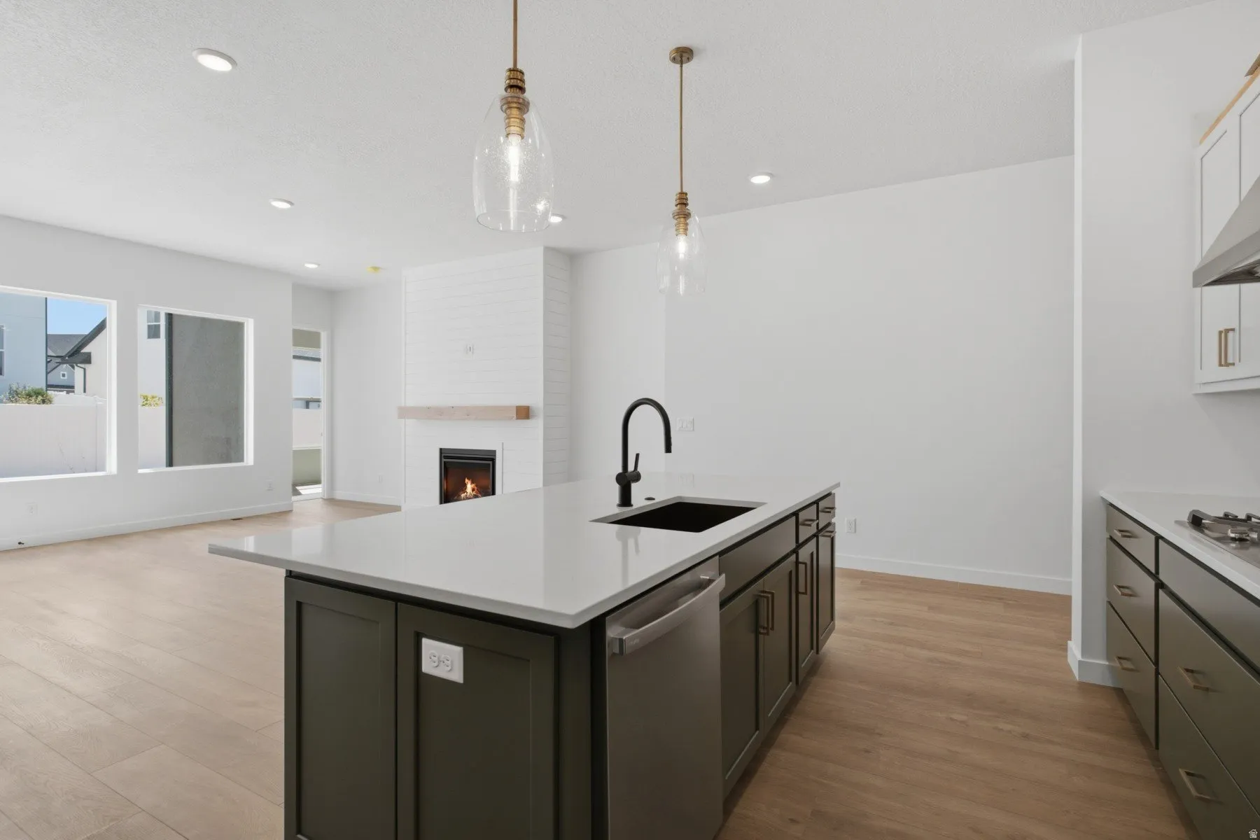 Kitchen island with a light-toned countertop and dark cabinetry, featuring a built-in sink and stainless steel dishwasher