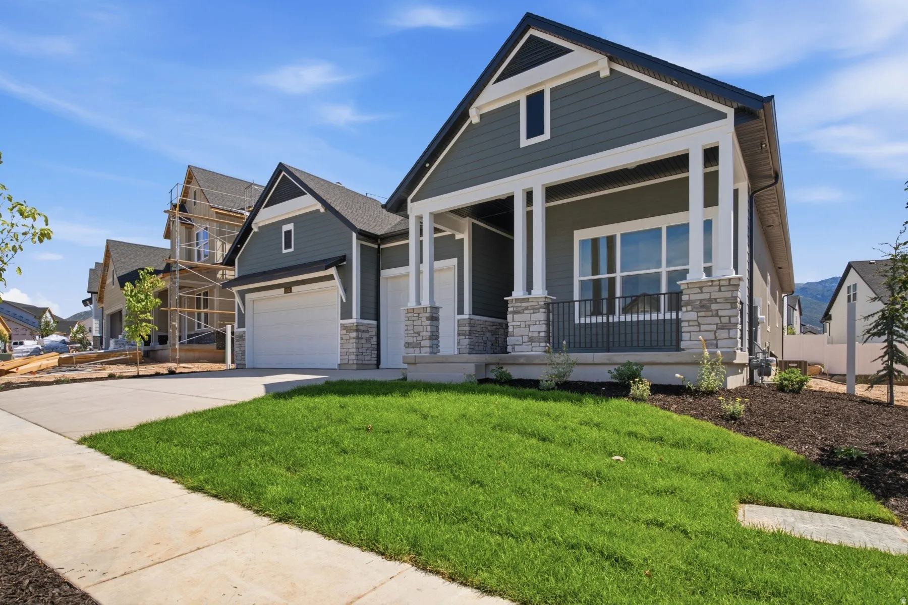 Contemporary home exterior featuring a covered porch with stone pillars, horizontal siding, a two-car garage, and a manicured lawn