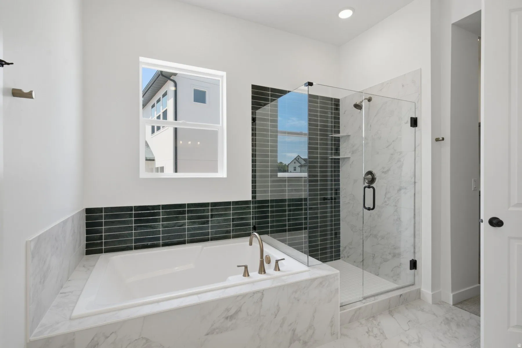 Built-in soaking tub with deck-mounted faucet, glass-enclosed shower with tile surround, and recessed lighting