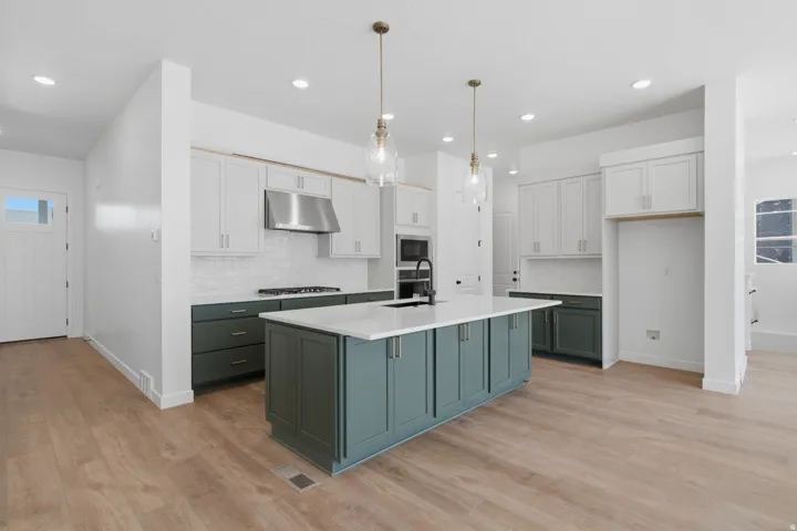Open-concept kitchen featuring an expansive island with a light-toned countertop, two-tone cabinetry, wood-finish flooring, and recessed lighting