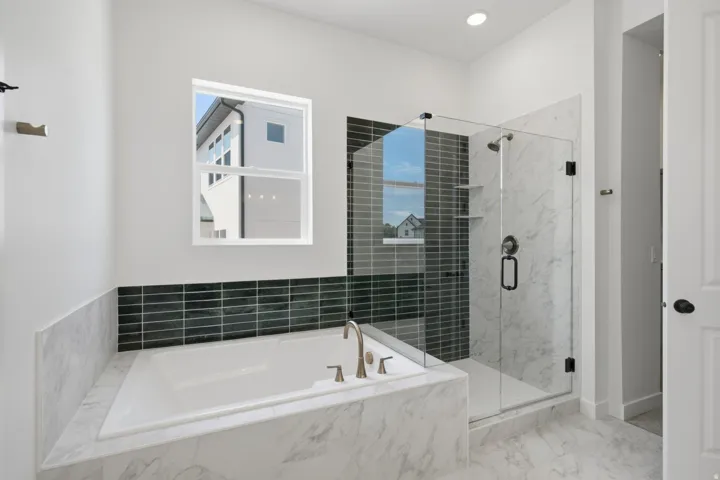 Built-in soaking tub with deck-mounted faucet, glass-enclosed shower with tile surround, and recessed lighting