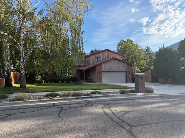 Brick and wood-sided exterior with an attached garage, featuring a tiled roof and mature landscaping