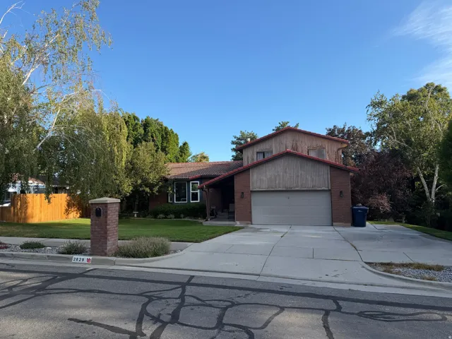 Brick and wood-sided exterior with a tile roof, an integrated garage, a concrete driveway, and mature landscaping
