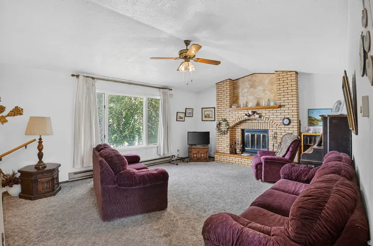 Brick fireplace with an arched opening, large windows providing natural light, and a ceiling fan with integrated lighting