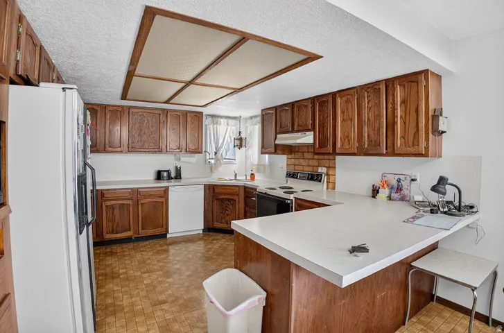 U-shaped kitchen featuring wood cabinetry, light-toned countertops, a built-in dishwasher, and a brick-patterned backsplash