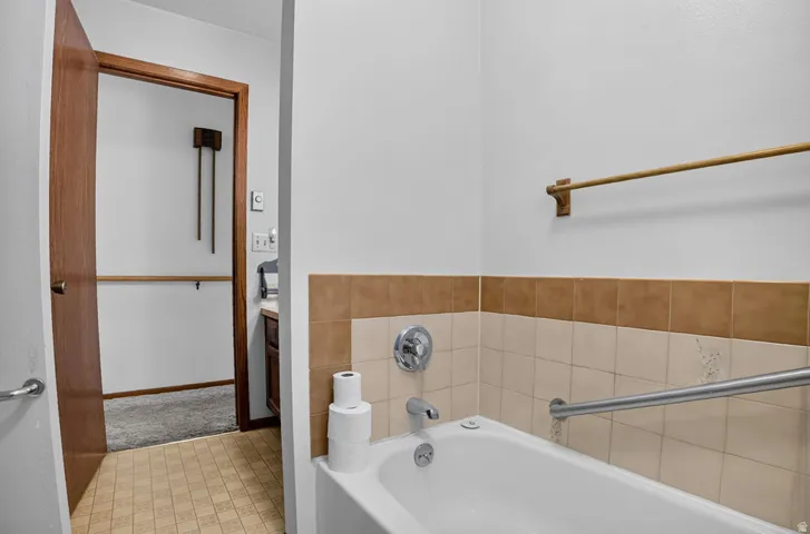 White bathtub with a chrome faucet, light-toned wall tile, and a metal grab bar