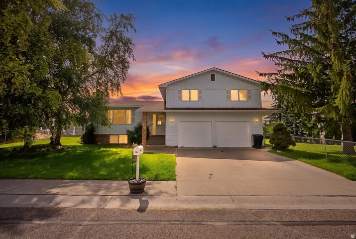 Two-story exterior with light-colored siding, an attached two-car garage, mature trees, and a concrete driveway