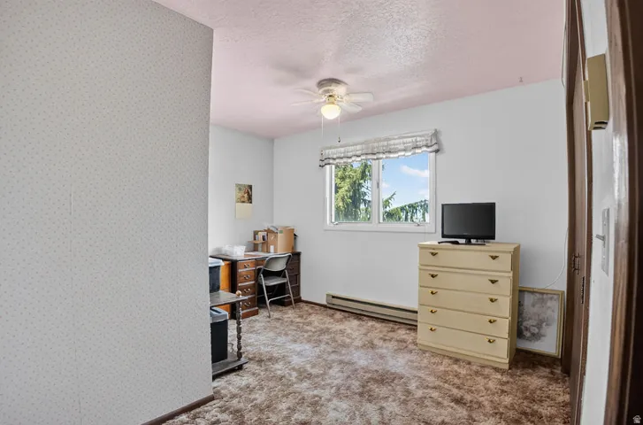 Window with exterior foliage, ceiling fan, and wall-mounted baseboard heater