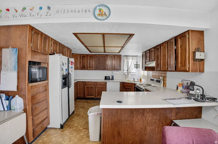 Galley kitchen featuring wood-finish cabinetry, solid surface countertops, and white appliances