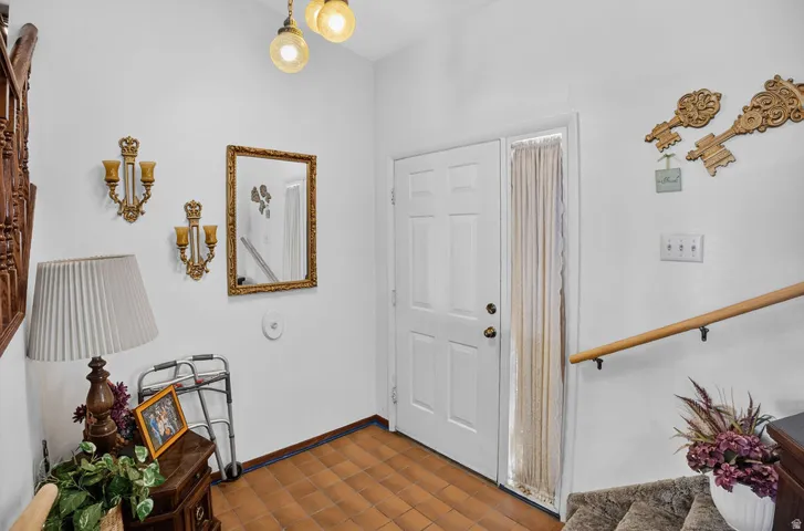 Panel door entry with a sidelight, ceramic tile flooring, and a wooden handrail