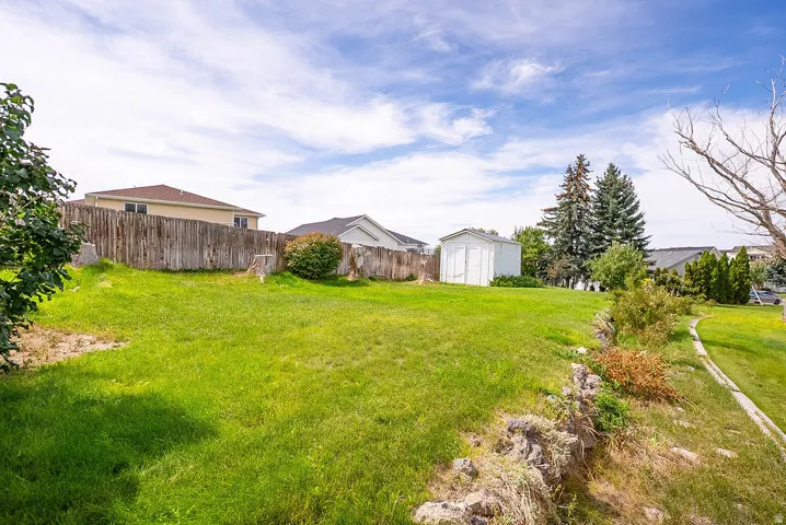 Expansive green space featuring a wood fence, mature trees, and a storage shed