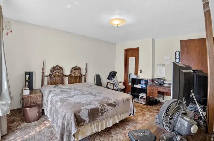Spacious primary bedroom with ornamental wood headboard, hardwood flooring, ceiling-mounted light fixture, and ample natural light from multiple windows