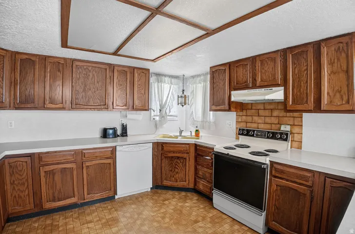 U-shaped kitchen featuring wood-finish cabinetry, white countertops, a built-in dishwasher, and a tile backsplash