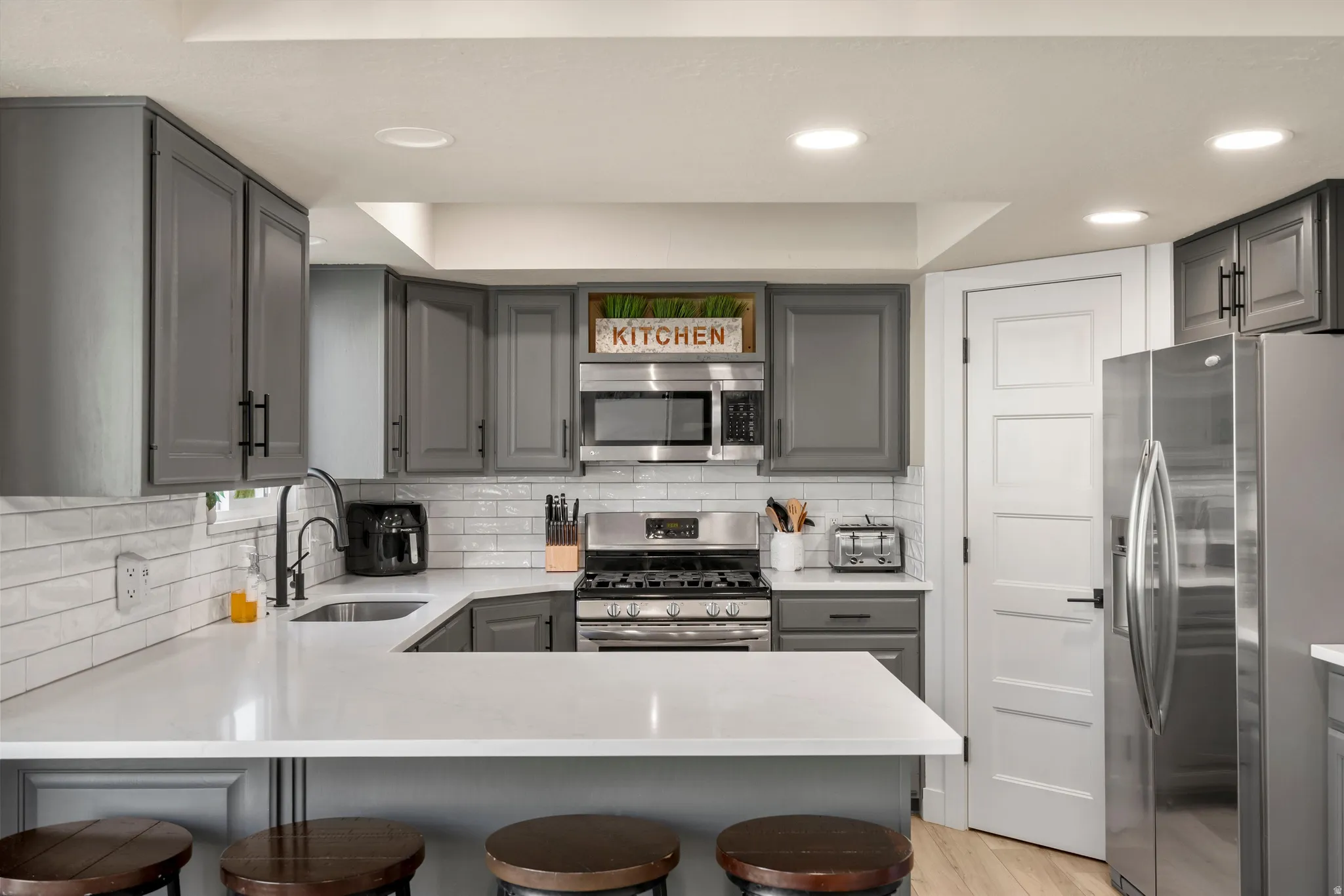 Modern kitchen featuring gray cabinetry, white subway tile backsplash, stainless steel appliances, white countertops, and recessed lighting