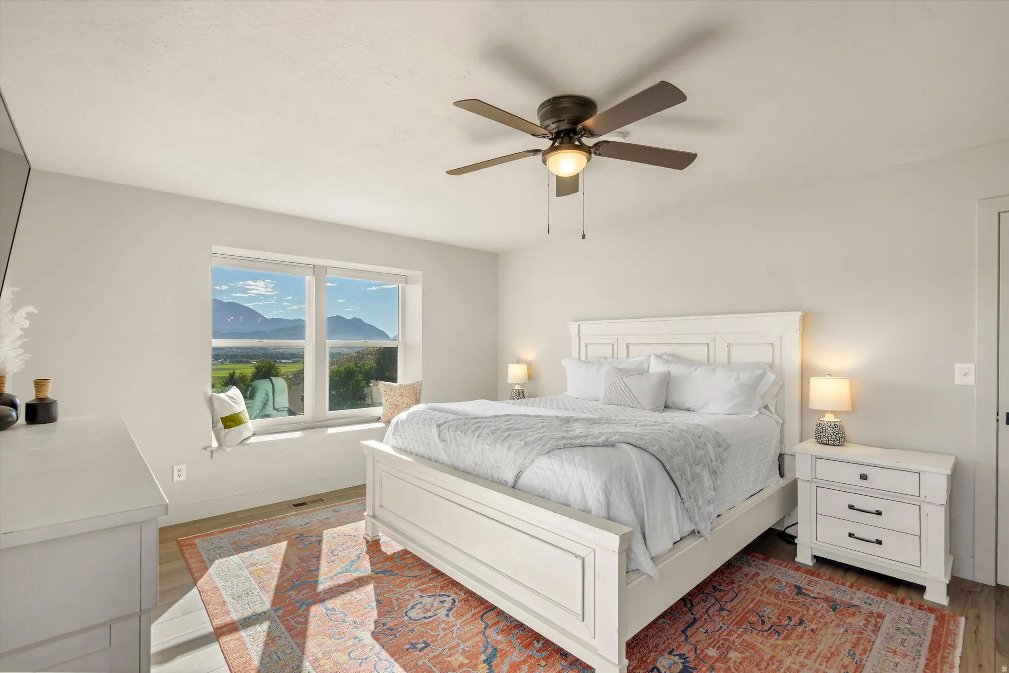 Light-toned walls, wood-finish flooring, recessed window ledge, ceiling fan with integrated lighting, and a paneled door