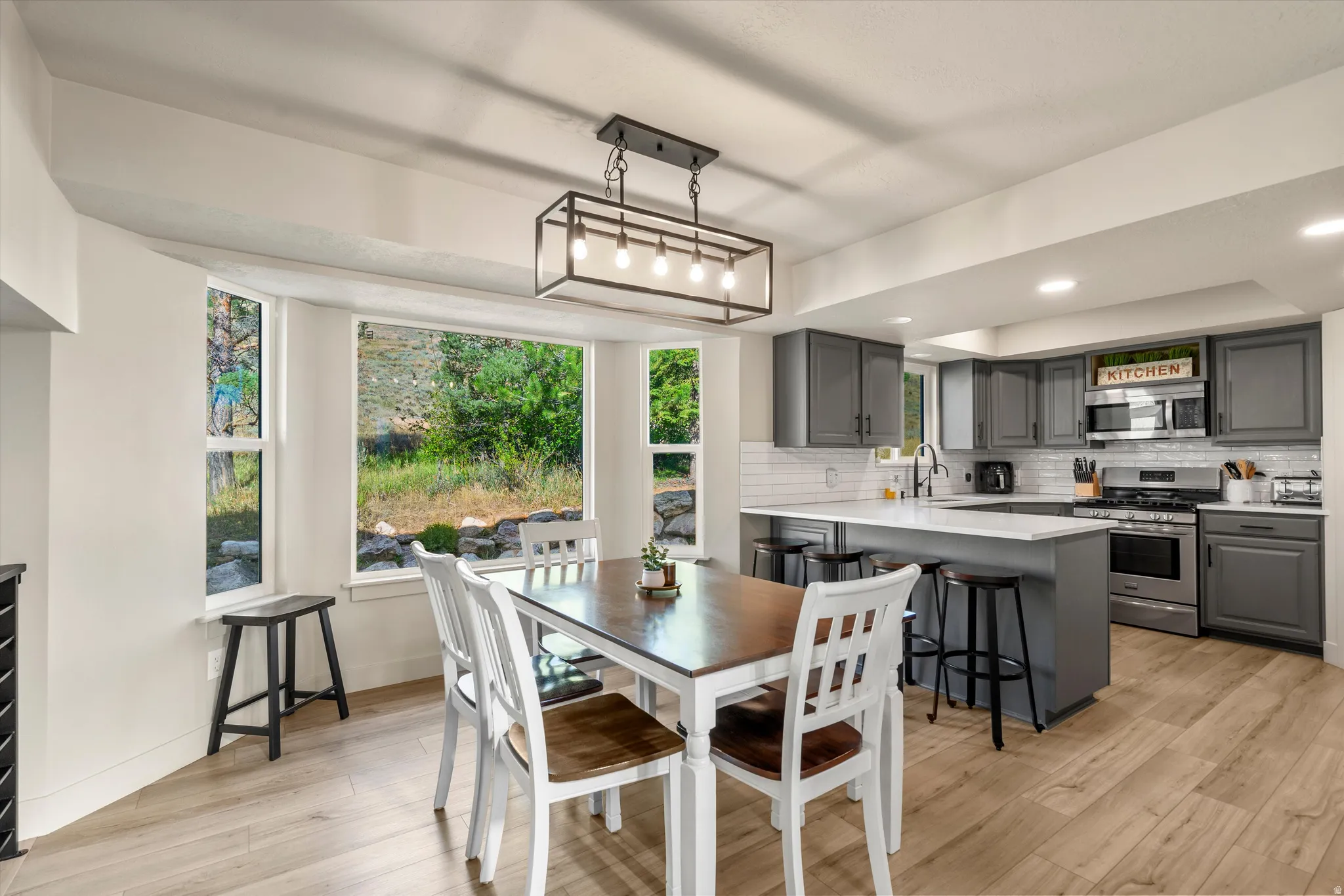 Kitchen with grey cabinetry, stainless steel appliances, white subway tile backsplash, and light wood-finish flooring