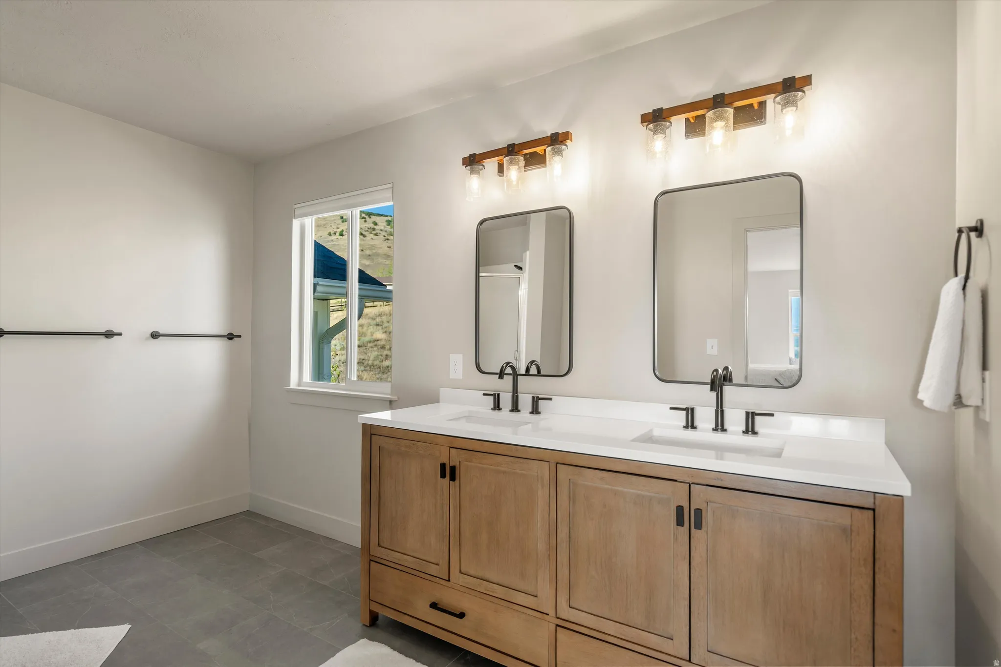 Dual vanity with wood-finish cabinetry, white countertops, matte black faucets, and rectangular framed mirrors