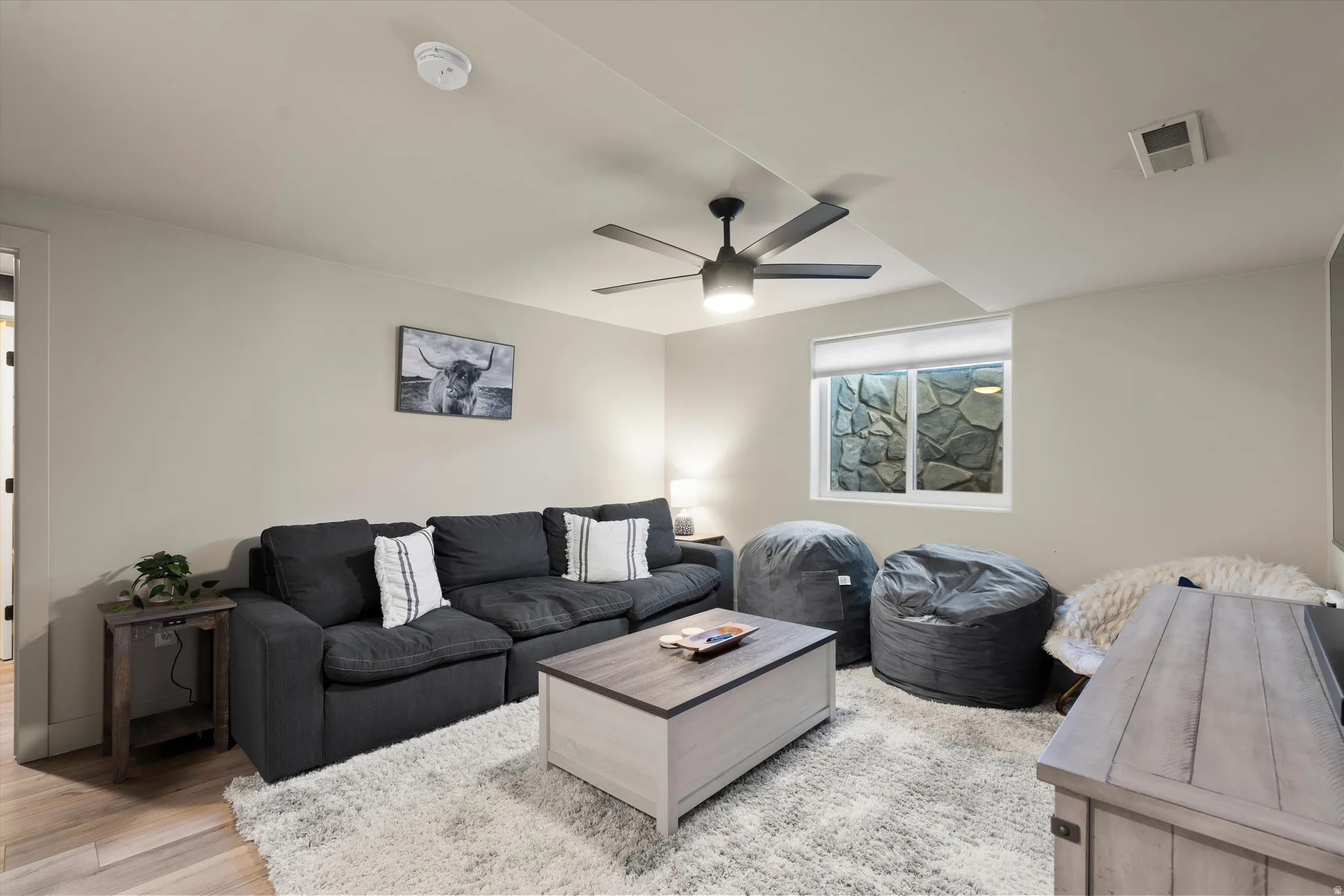 Recessed lighting, ceiling fan with integrated light, wood-finish flooring, and a stone-lined window well