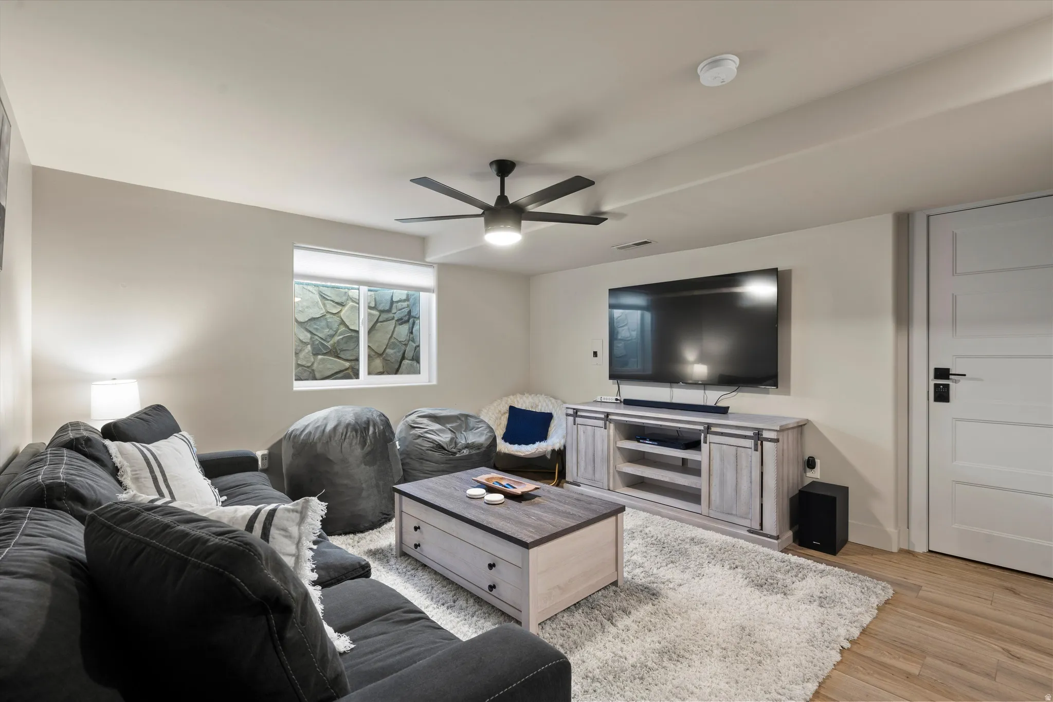 Recessed lighting, ceiling fan, wood-finish flooring, accent window with stone feature, and a four-panel door with matte black hardware